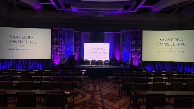Professional event setup featuring Saavedra Consulting branding with sophisticated staging, lighting, and audio-visual technology